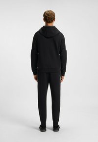 Czarna bluza z kapturem, z rękawami raglanowymi i ściągaczami, w połączeniu z dopasowanymi czarnymi spodniami. Gładki materiał i minimalistyczny design.