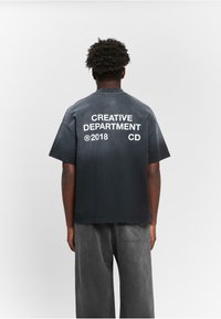 Schwarzes Baumwoll-T-Shirt mit Rundhalsausschnitt und kurzen Ärmeln, das auf der Rückseite auffälligen weißen Text zeigt: "CREATIVE DEPARTMENT", "CD" und "2018".