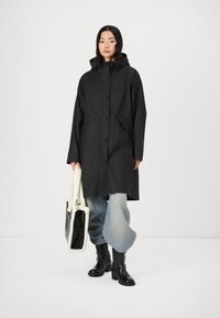 Svart vattentät jacka med huva, med en lång design, tryckknappar och sidofickor, i kombination med ljusblå vida jeans och en toteväska.