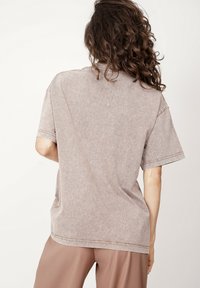 Krótki rękaw, luźna koszulka w kolorze jasnobeżowym z teksturowanym wykończeniem, widocznymi przeszyciami i casualową, oversize'ową sylwetką.
