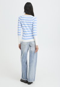 Haut à manches longues rayé bleu et blanc avec un col rond, associé à un jean large bleu clair. Texture de tissu lisse, coupe décontractée.