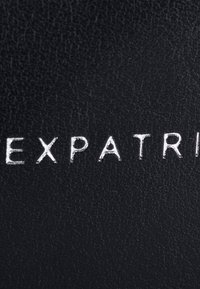 Black leather with a textured surface, featuring embossed silver lettering spelling "EXPATRIATE." Clear, modern design.