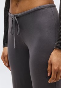 Κοντινό πλάνο ενός ατόμου που φοράει γκρι παντελόνια με κορδόνι και μαύρο ριμπ μπλούζα με μακριά μανίκια, εμφανίζοντας τη μέση και τα χέρια χαλαρά δίπλα στο σώμα.