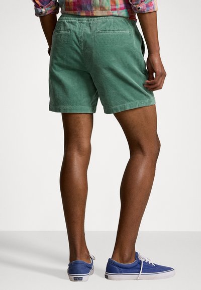 Shorts en velours côtelé vert avec une coupe décontractée, dotés de deux poches arrière et d'un tissu texturé. Assortis à des baskets en toile bleues.