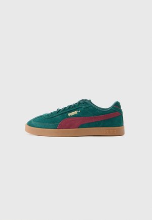 Sneaker en suède vert et marron de la marque Puma avec une semelle en gomme, logo sur le côté et design à lacets, présenté de profil sur fond blanc.