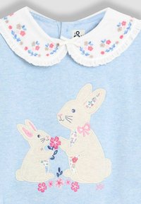 Hellblauer Pullover mit einem gestickten Design von zwei Hasen, versehen mit einem weißem Kragen, der mit floralen Mustern geschmückt ist.