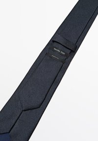 Tmavě modrá kravata s texturovaným povrchem a špičatým koncem. Štítky: „Massimo Dutti“ a „Vyrobeno v Itálii“, přišité na zadní straně.