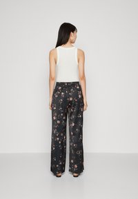 Pantaloni a gamba larga neri con una texture lucida, vita elastica e dettagli floreali in tonalità di rosa e verde.