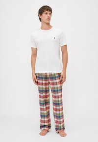 T-shirt en coton blanc avec un petit logo, associé à un pantalon en flanelle à carreaux rouge, bleu, jaune et vert. Coupe décontractée et texture légère.