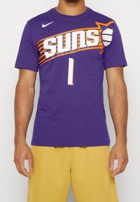 Lilla T-shirt med orange og hvid "Suns" grafik og nummer "1" på forsiden. Fremstillet af blød bomuld; design med rund hals.