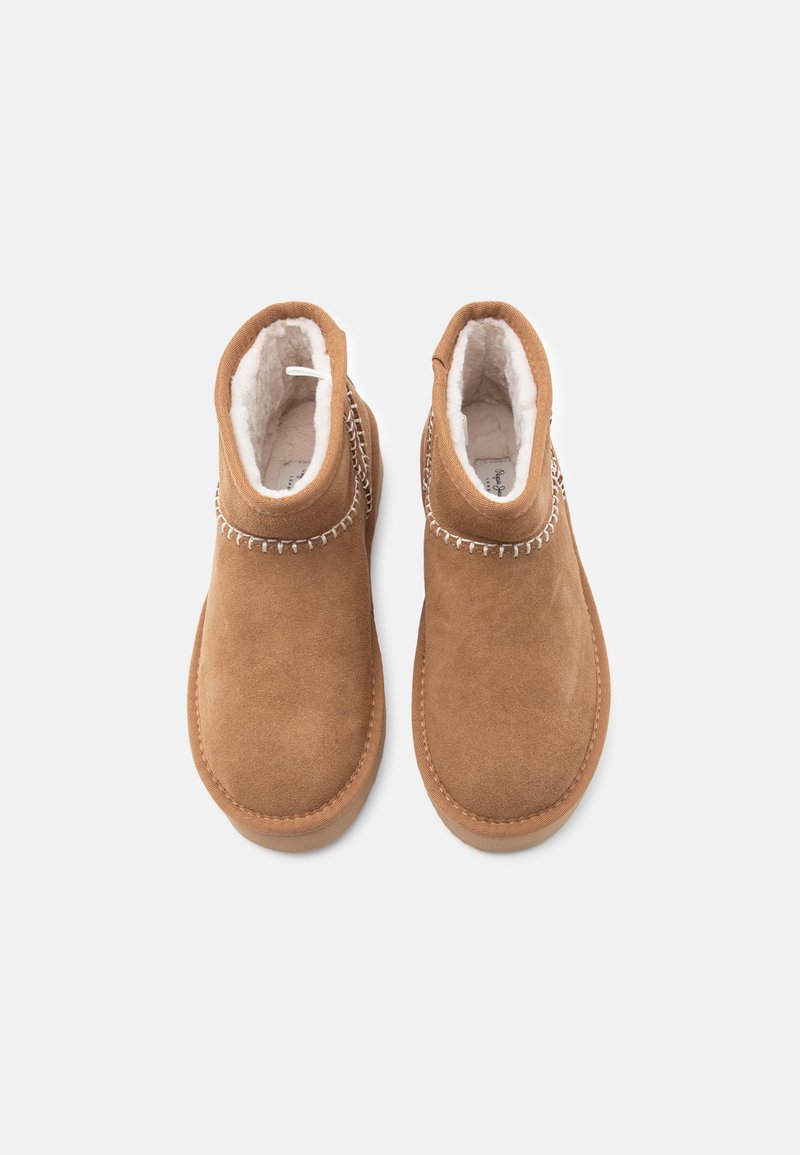 Bottines en suede marron avec une doublure intérieure douce, présentant un motif de couture décoratif autour de la cheville et un bout arrondi.