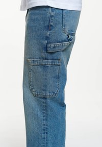 Blå denimjeans med rak benprofil, en bakfickapåse och svaga bleknade detaljer. Tyget har en klassisk texturerad yta.