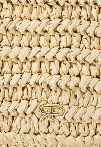 Natural woven straw material with a textured surface in light beige. Features a gold logo accent near the bottom.