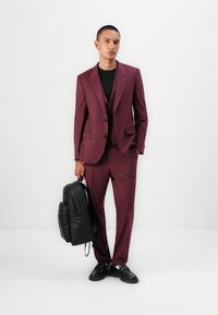 Bordeaux pak met een fitted design, gecombineerd met een zwart t-shirt. Accessoires zijn een zwarte leren rugzak en zwarte schoenen.