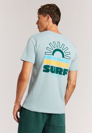 Lichtblauw katoenen t-shirt met een grafisch ontwerp op de achterkant met de tekst "Good Times Sunset Surf" in groenblauw en geel, korte mouwen.