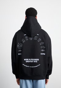 Black hoodie with a large back print featuring white text and designs. Material appears soft with a large, adjustable hood and ribbed cuffs.
