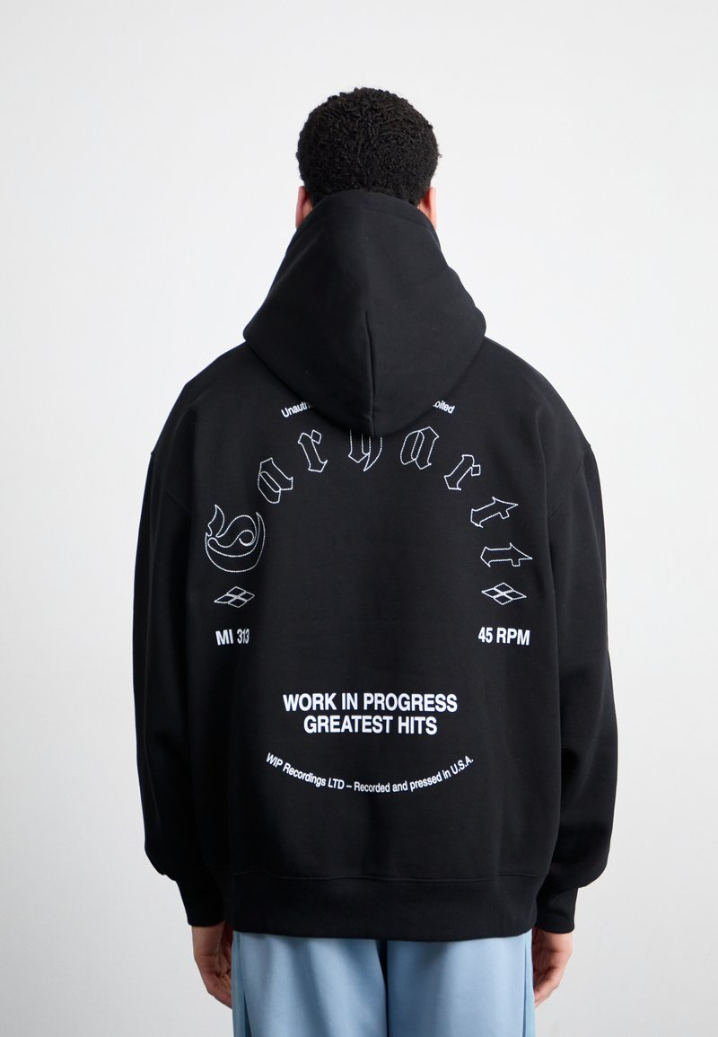 Black hoodie with a large back print featuring white text and designs. Material appears soft with a large, adjustable hood and ribbed cuffs.