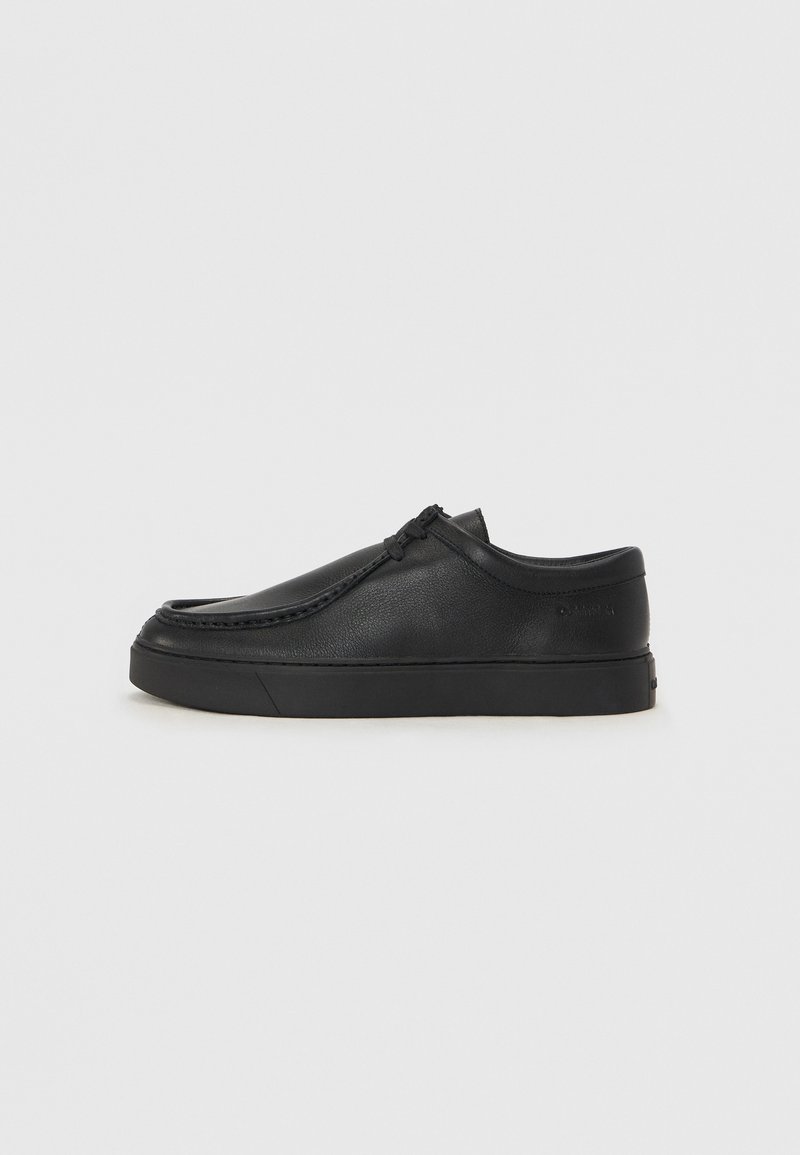 Sapata slip-on de couro preto com biqueira arredondada, detalhes cosidos e sola de borracha preta. Textura suave com design minimalista.