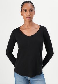 Svart langermet V-hals T-skjorte laget av mykt stoff, med en avslappet passform og synlige sømdetaljer, sammen med lyseblå jeans.