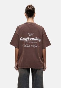 Brązowy, oversize t-shirt z krótkim rękawem. Posiada biały napis "Goodfornothing" oraz grafikę motyla na plecach. Teksturowana tkanina.