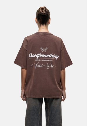 Braunes oversized T-Shirt mit kurzen Ärmeln. Auf der Rückseite befindet sich der weiße Text "Goodfornothing" sowie eine Schmetterlingsgrafik. Strukturiertes Material.