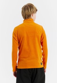Oranje fleece pullover met een hoge kraag, lange mouwen en een gestructureerde afwerking. Bevat een zwart logo-label aan de onderrand.