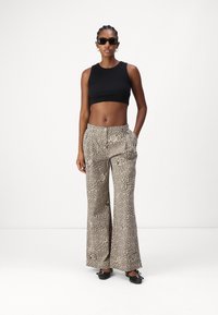 Schwarzes Cropped Top, weite Leopardenmuster-Hosen in Beige mit braunen Flecken, glatter Stoff, mit seitlichen Taschen, getragen mit schwarzen Ballerinas und Sonnenbrille.