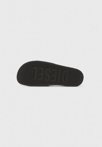 Semelle de chaussure en caoutchouc noir avec surface texturée ; comporte la marque "DIESEL" en relief et des bords lisses. Design simple et plat sans motifs distincts.
