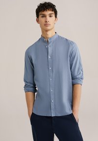 Svetlo modra srajca s mandarin ovratnikom, dolgi rokavi, zloženimi do komolcev, in naguban površin. V kombinaciji s temnimi hlačami.