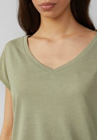 Jasnozielona koszulka typu V-neck z krótkimi rękawami, wykonana z miękkiego materiału. Charakteryzuje się gładką fakturą i luźnym krojem.