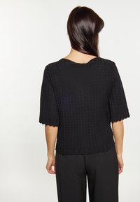 Maglione nero lavorato a maglia con un motivo testurizzato, maniche corte a forma di scalloped e un ampio scollo, abbinato a pantaloni neri larghi.