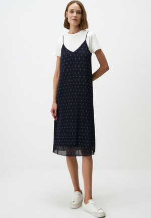 Abito slip blu navy con spalline sottili, caratterizzato da piccoli motivi bianchi. Indossato sopra una t-shirt bianca e abbinato a sneakers bianche.