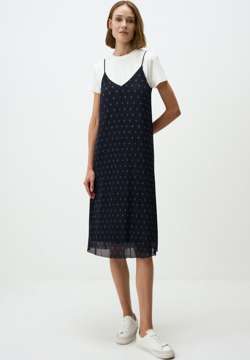 Marineblauwe slipdress met dunne bandjes, voorzien van kleine witte patronen. Draag het over een wit T-shirt en combineer het met witte sneakers.