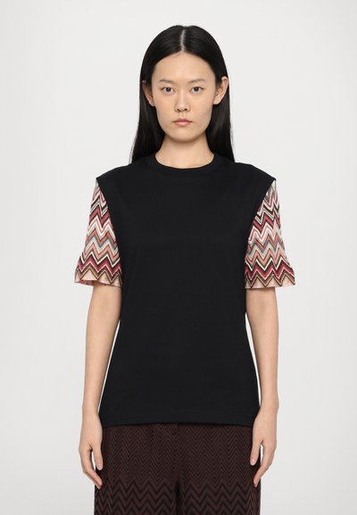 Zwarte t-shirt met korte mouwen, voorzien van patronen op de mouwen met zigzagontwerpen in roze, rood, goud en crème. Gladde textuur, ontspannen pasvorm.