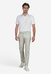 Witte polo met kraag met marineblauwe accenten, lichtbeige slim-fit broek en witte sneakers op een effen achtergrond.