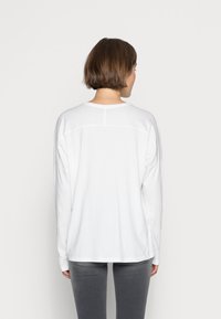 Langärmliges weißes T-Shirt aus weicher Baumwolle, mit Rundhalsausschnitt, lockerer Passform und dezenten Nahtdetails auf der Rückseite.
