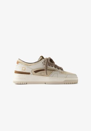 Beige lage sneaker met dikke zool, suède- en leren panelen en dikke bruine veters, van opzij getoond tegen een witte achtergrond.