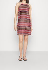 Robe à col halter avec un motif en zigzag rouge, rose et noir. Design ajusté avec un ourlet à hauteur du genou et un tissu léger.