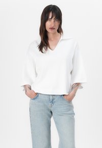Bílý krátký rukáv svetr ve tvaru V vyrobený z jemné pleteniny, kombinovaný s světle modrými džíny rovného střihu. Jednoduchý design s minimálními detaily.