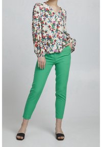 Floral patterned blouse with balloon sleeves, cream background. Green slim-fit pants, ankle length, paired with black slide sandals.