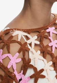Hæklet top med et åbent design med brune, lyserøde og cremefarvede blomstermotiver; tekstureret garn med en blød, taktil kvalitet.