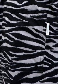 Tissu imprimé zèbre noir et gris avec une poche patch cousue comportant une petite étiquette de marque blanche sur le bord droit.