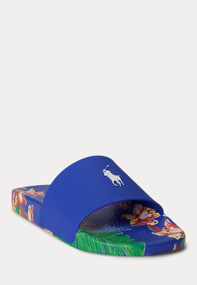 Niebieska klapka na obcasie z kwiatowym wzorem na podeszwie i srebrnym logo gracza polo na szerokim pasku, widok pod kątem na białym tle.