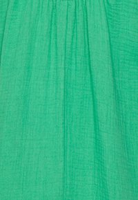 Zielona tkanina o teksturowanym wykończeniu, z pionowymi plisami tworzącymi falujący wygląd. Miękki i lekki materiał.