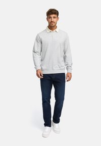 Grå sweatshirt med hvid krave, lange ærmer, ribbede manchetter og kant. Sammen med mørkeblå jeans og hvide sneakers. Stående position.