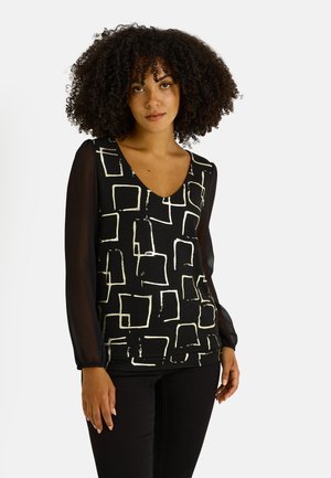 Blusa negra con patrones cuadráticos abstractos en blanco, escote en forma de V y mangas largas transparentes. La tela es suave con un ajuste ligeramente estructurado.