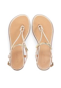 Sandales plates beige avec une semelle en cuir lisse, dotées de brides métalliques et d'un design noué. Quincaillerie dorée près de la cheville.