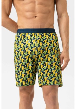Torse masculin mince portant un short bleu marine avec un motif répétitif de boissons tropicales jaunes et vertes, debout sur un fond blanc.