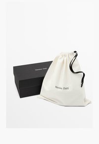 Borsa in cotone con coulisse color crema con la scritta "Massimo Dutti" stampata in nero, abbinata a una scatola rettangolare nera, design minimalista.