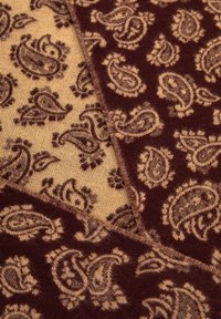 Il tessuto color tan e borgogna presenta motivi paisley, con una texture morbida e sezioni di colori contrastanti, che mettono in mostra dettagli intricati.